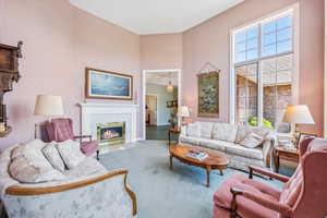 Living room featuring a high ceiling, carpet, a tiled fireplace, and plenty of natural light