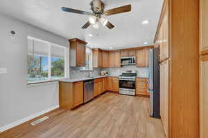 Kitchen with stainless steel appliances, ceiling fan, tasteful backsplash, light stone countertops, and light wood-type tile flooring