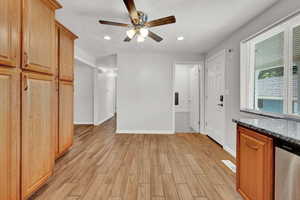 Kitchen with light hardwood / wood-style tile floors, dark stone counters, ceiling fan, and stainless steel dishwasher