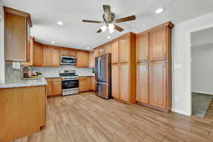 Kitchen with stainless steel appliances, backsplash, ceiling fan, light stone countertops, and sink