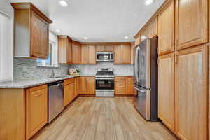 Kitchen featuring light stone countertops, light hardwood / wood-style tile flooring, stainless steel appliances, backsplash, and sink