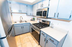 Kitchen with sink, grey cabinets, light tile floors, and stainless steel appliances