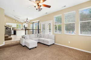 Living room featuring ceiling fan with notable chandelier, light colored carpet, and lofted ceiling