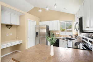 Kitchen featuring vaulted ceiling, white cabinets, and appliances with stainless steel finishes