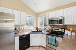 Kitchen with stainless steel appliances, white cabinetry, sink, light tile floors, and lofted ceiling