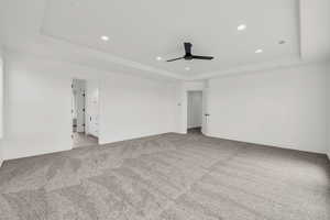 Carpeted empty room with ceiling fan and a raised ceiling