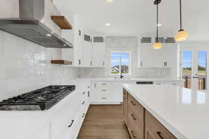 Kitchen featuring dark wood-type flooring, decorative backsplash, wall chimney range hood, and a healthy amount of sunlight