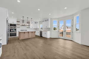 Kitchen featuring wall chimney range hood, a kitchen island, french doors, appliances with stainless steel finishes, and light hardwood / wood-style floors