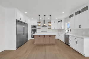 Kitchen featuring light wood-type flooring, built in appliances, tasteful backsplash, and a kitchen island