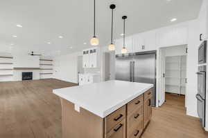 Kitchen featuring light hardwood / wood-style flooring, pendant lighting, white cabinets, a kitchen island, and built in appliances