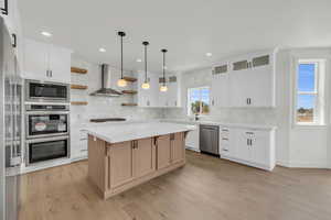 Kitchen with appliances with stainless steel finishes, wall chimney exhaust hood, light wood-type flooring, and tasteful backsplash