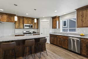 Kitchen featuring light hardwood / wood-style floors, pendant lighting, a kitchen island, sink, and appliances with stainless steel finishes