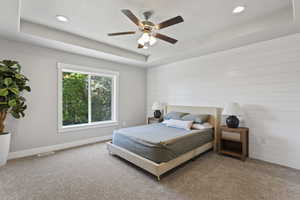 Bedroom with ceiling fan, a tray ceiling, and carpet floors