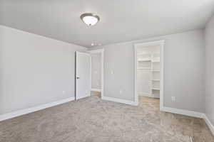 Unfurnished bedroom featuring light carpet, a spacious closet, and a closet