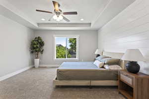 Carpeted bedroom with a raised ceiling and ceiling fan