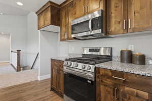 Kitchen featuring light carpet, light stone countertops, and stainless steel appliances