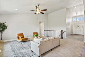 Carpeted living room featuring high vaulted ceiling and ceiling fan with notable chandelier