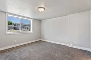 Spare room featuring a textured ceiling and dark carpet