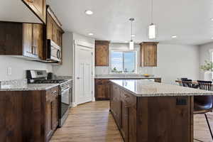 Kitchen featuring decorative light fixtures, light stone counters, light hardwood / wood-style flooring, a kitchen island, and stainless steel appliances