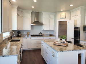 Kitchen featuring white cabinets, wall chimney range hood, and a center island