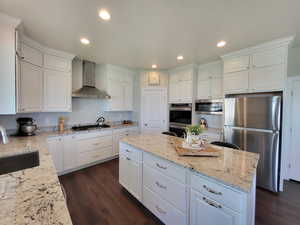 Kitchen featuring white cabinetry, dark wood-type flooring, appliances with stainless steel finishes, wall chimney exhaust hood, and sink