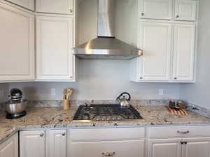 Kitchen featuring light stone countertops, white cabinetry, wall chimney exhaust hood, and stainless steel gas cooktop