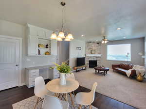 Dining room featuring a stone fireplace, dark hardwood / wood-style flooring, and ceiling fan with notable chandelier