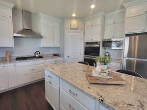 Kitchen featuring stainless steel appliances, dark wood-type flooring, light stone counters, wall chimney exhaust hood, and white cabinets