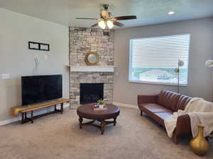 Living room with a stone fireplace, ceiling fan, carpet floors, and a textured ceiling