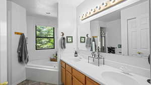 Bathroom featuring a relaxing tiled bath, vanity with extensive cabinet space, double sink, and tile flooring