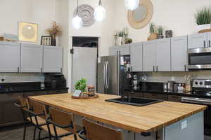 Kitchen with decorative light fixtures, a kitchen island, backsplash, wooden counters, and appliances with stainless steel finishes