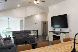 Living room with high vaulted ceiling, dark wood-type flooring, and ceiling fan with notable chandelier