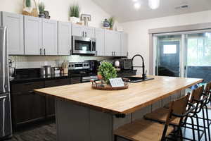 Kitchen featuring appliances with stainless steel finishes, a kitchen island with sink, backsplash, and a breakfast bar area