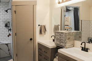 Bathroom featuring a tile shower and dual vanity