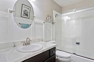 Full bathroom featuring a textured ceiling, combined bath / shower with glass door, toilet, and vanity with extensive cabinet space