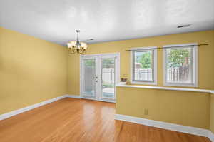 Spare room with a notable chandelier, light hardwood / wood-style flooring, and french doors