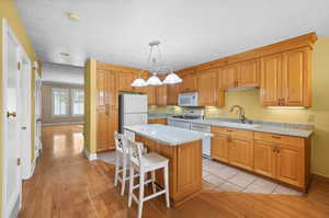 Kitchen with white appliances, light wood-type flooring, pendant lighting, a center island, and sink