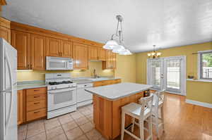 Kitchen featuring a center island, hanging light fixtures, white appliances, a chandelier, and sink