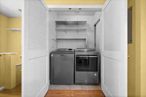 Clothes washing area with washer and clothes dryer and light hardwood / wood-style floors