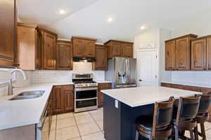 Kitchen featuring stainless steel appliances, vaulted ceiling, backsplash, a center island, and sink