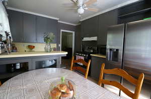 Kitchen with ceiling fan, crown molding, stainless steel refrigerator with ice dispenser, black / electric stove, and tile countertops