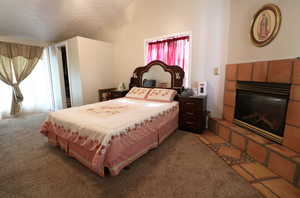 Bedroom with vaulted ceiling, carpet, and a tiled fireplace