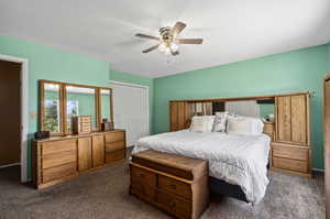 Bedroom with ceiling fan, a closet, and dark colored carpet