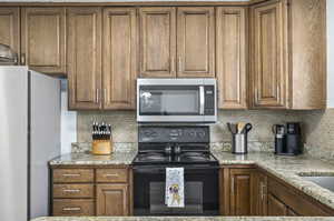 Kitchen with backsplash, light stone counters, black electric range oven, and fridge