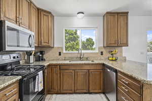 Kitchen featuring light stone countertops, stainless steel appliances, sink, tasteful backsplash, and light tile floors