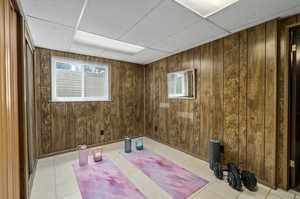 Interior space with light tile floors, plenty of natural light, a paneled ceiling, and wood walls