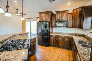 Kitchen with sink, light tile patterned floors, light stone counters, black appliances, and decorative light fixtures