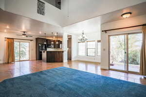 Unfurnished living room featuring ceiling fan with notable chandelier, tile patterned floors, and a high ceiling