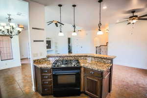 Kitchen featuring gas stove, decorative light fixtures, dark brown cabinets, light stone countertops, and ceiling fan with notable chandelier