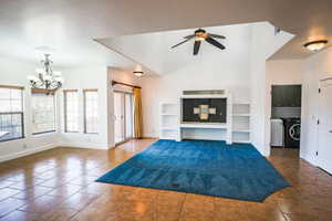 Unfurnished living room with ceiling fan with notable chandelier, built in features, independent washer and dryer, and dark tile patterned floors